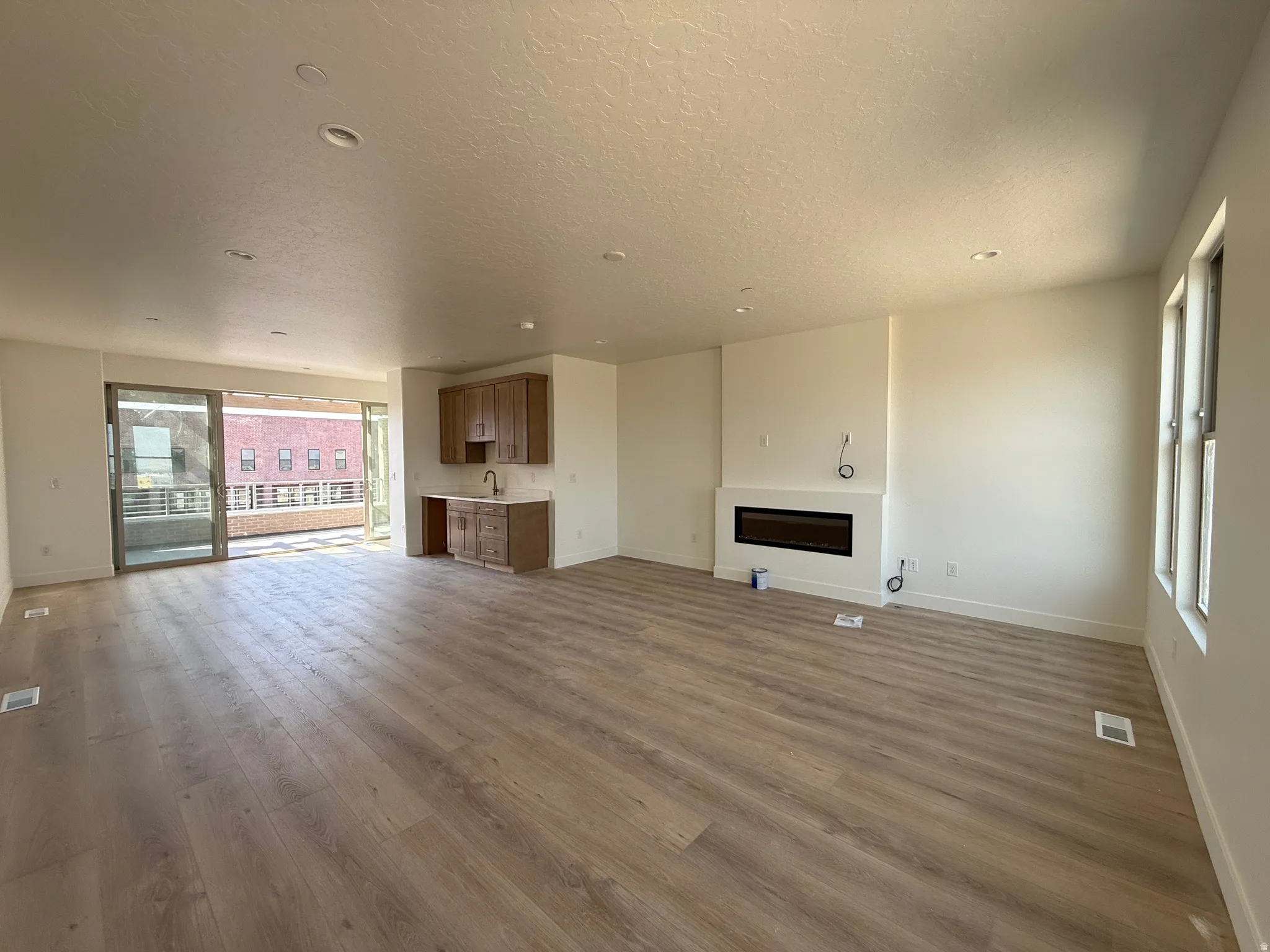 Spacious open-concept room featuring light wood-finish flooring, recessed lighting, and a contemporary linear electric fireplace
