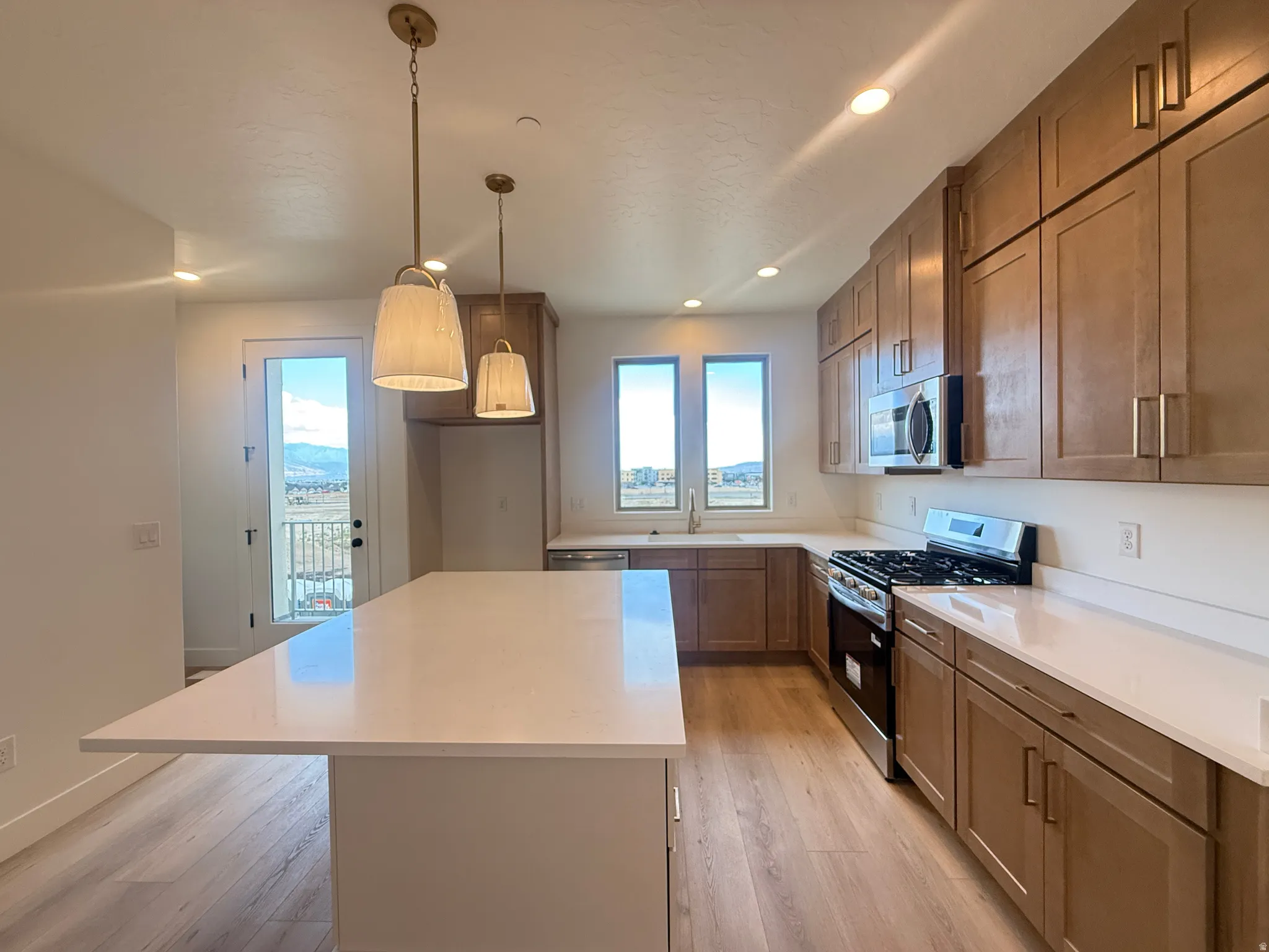 Modern kitchen featuring an expansive island with a light-toned countertop, wood-finish flooring, recessed lighting, and a stainless steel appliance suite