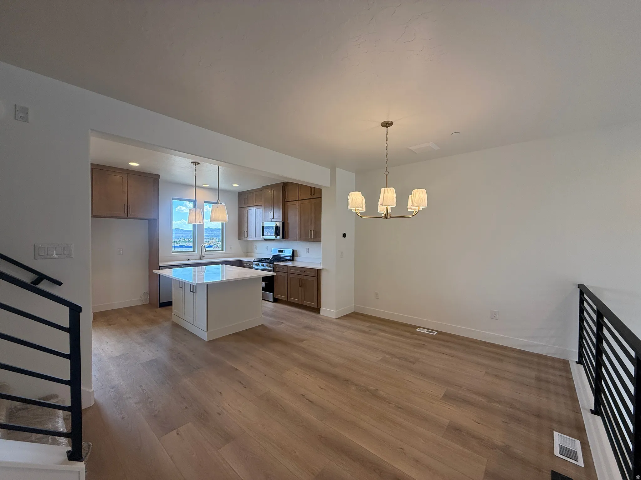 Open-concept living space featuring wood-finish flooring, a modern kitchen with a central island and pendant lighting, and a contemporary chandelier