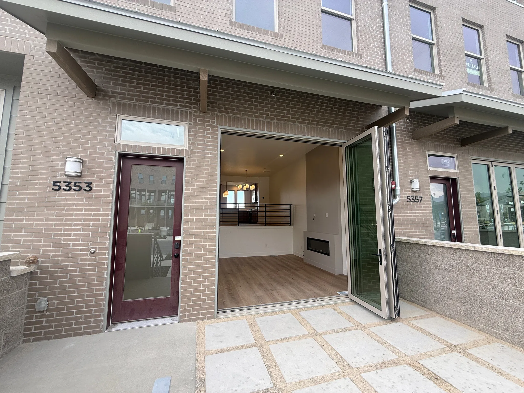 Patio entrance featuring accordion-style glass doors, light brick facade, and concrete pavers