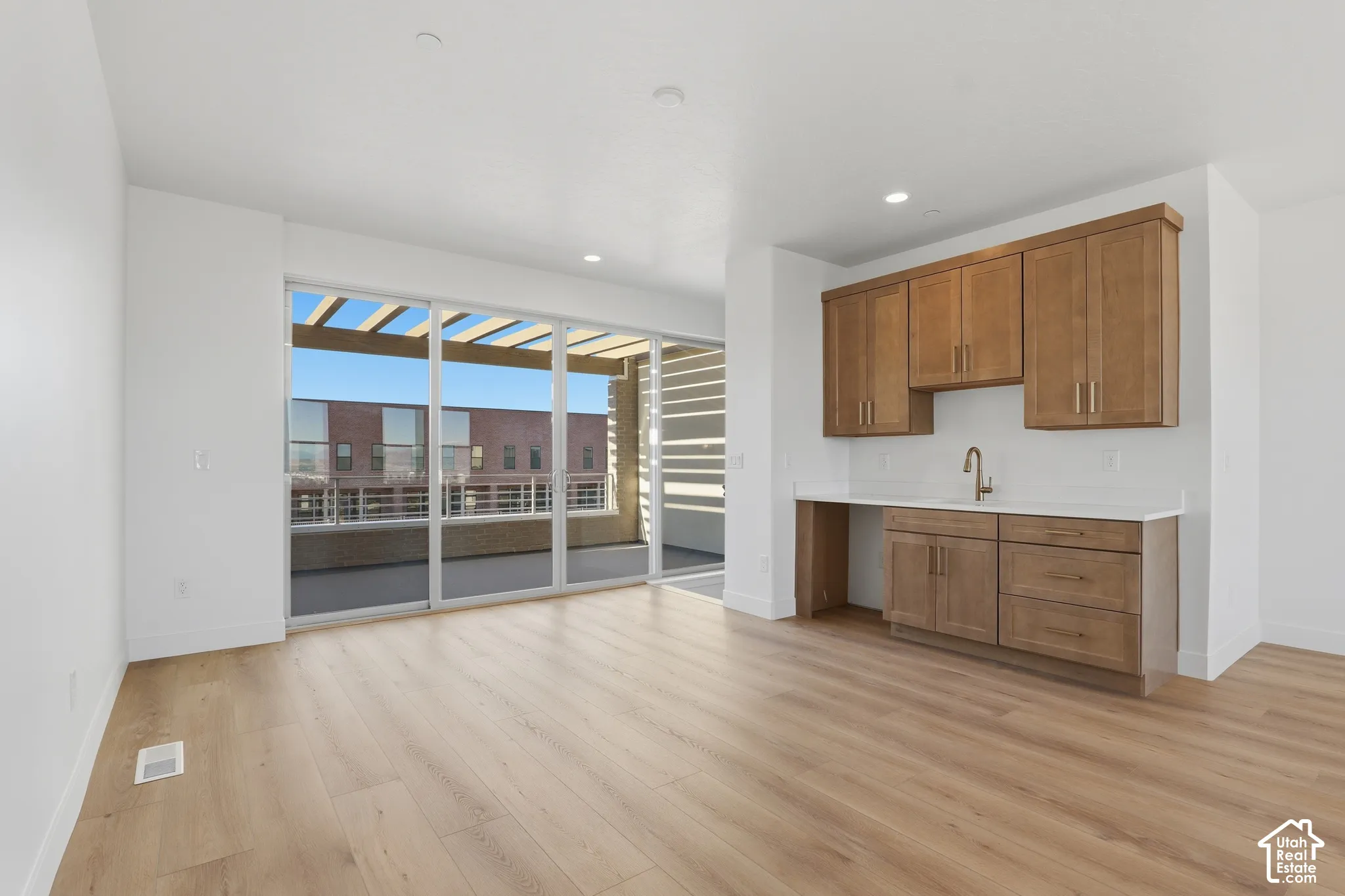 Wood-finish flooring, built-in cabinetry with stone-surface counters, stainless steel hardware, undermount sink with gooseneck faucet, and oversized sliding glass doors leading to a covered balcony