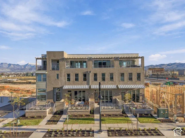 Multi-story townhouse exterior featuring a textured stucco facade, metal-roofed awnings, private ground-level patios, and a top-level covered terrace with mountain scenery