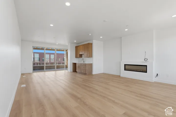 Open-concept interior featuring light-tone wood-finish flooring, recessed lighting, a linear built-in fireplace, natural wood cabinetry, and floor-to-ceiling glass sliding doors