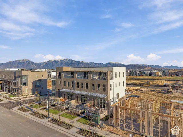 Three-story masonry exterior featuring expansive upper-level balconies, metal awnings, paved ground-level patios, and a prominent mountain backdrop