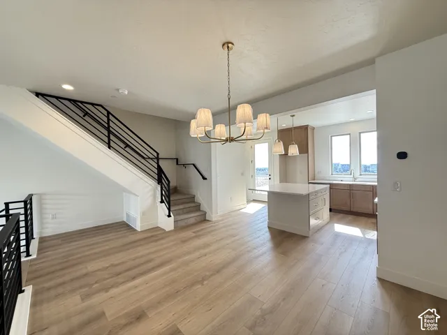 Wood-finish flooring, contemporary black metal railings, a modern brass chandelier, and a kitchen island with pendant lighting