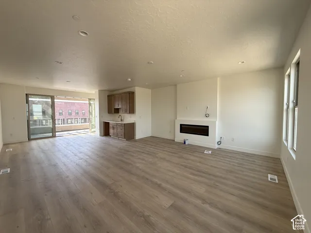 Spacious open-concept room featuring light wood-finish flooring, recessed lighting, and a contemporary linear electric fireplace