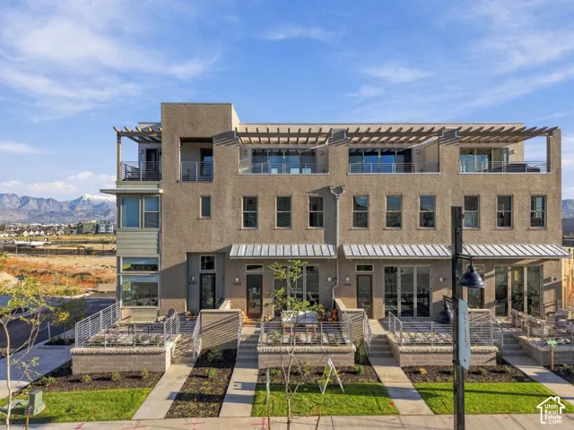 Multi-story exterior featuring masonry construction, metal-awning accents, top-level pergolas, metal railing balconies, and stone-retaining wall patios