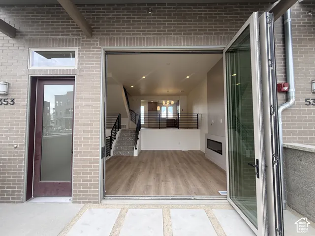 Expansive bi-fold glass doors open to a contemporary interior featuring wood-finish flooring, a linear fireplace, and a modern staircase with dark metal railings