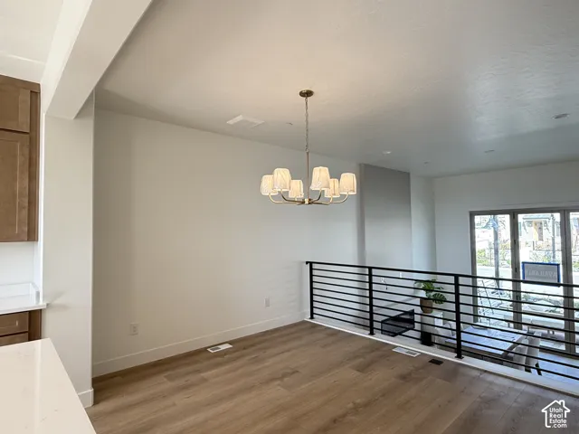 Brass chandelier with linen shades, wood-finish flooring, white walls, black horizontal bar railing, and large glass paneled doors