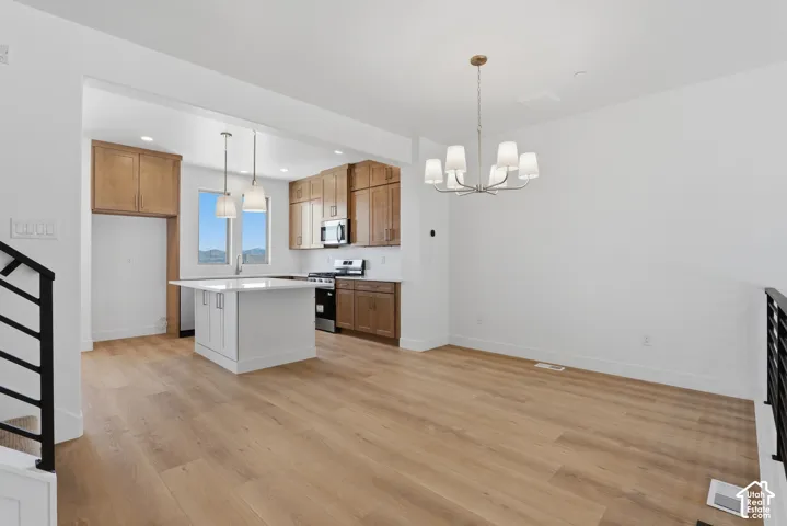 Open-concept kitchen and dining area featuring wood-finish flooring, shaker-style cabinetry, a central island with a white countertop, and multi-light fixtures