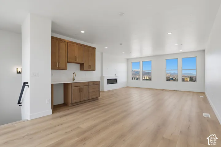 Open-concept space featuring wood-finish flooring, custom cabinetry with integrated sink, recessed lighting, wall-mounted electric fireplace, and large windows with mountain scenery