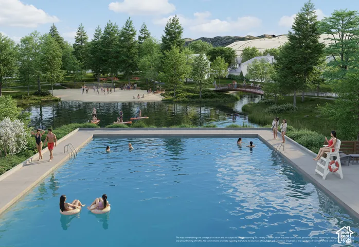Community swimming pool with surrounding concrete decking, green landscaping, and a natural body of water with a sandy beach