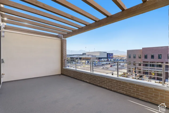 Covered terrace featuring a wooden pergola, brick exterior accents, metal railing, and mountain backdrop