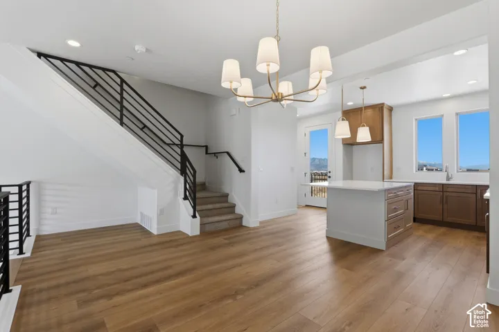 Open-concept interior featuring wood-finish flooring, a contemporary six-light chandelier, a staircase with matte black metal railings, and a kitchen island with a light-toned countertop