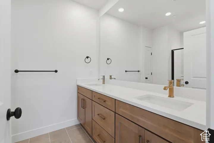 Dual-sink vanity with wood-finish cabinetry, white solid-surface countertop, gold-toned fixtures, and a wall-to-wall mirror