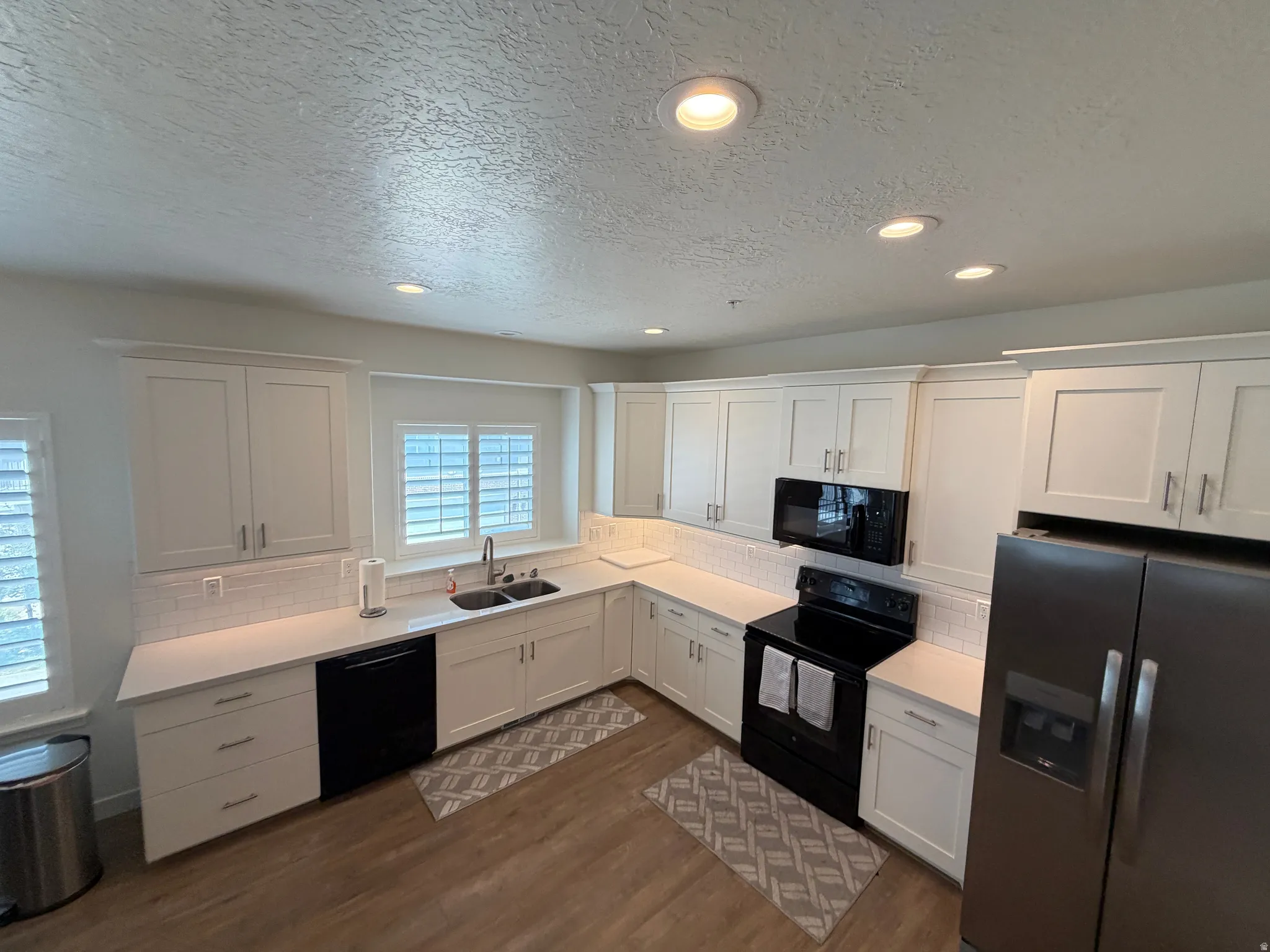 Contemporary kitchen featuring white shaker cabinetry, light-toned countertops, and wood-finish flooring