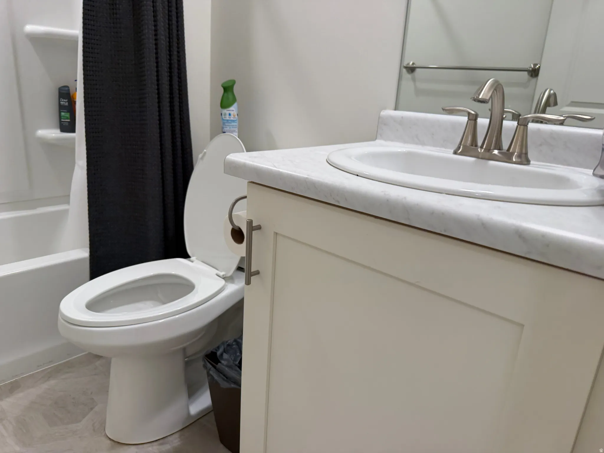 Bathroom featuring a white toilet, integrated sink with brushed nickel faucet, light-toned vanity with shaker-style door, and tub/shower combination