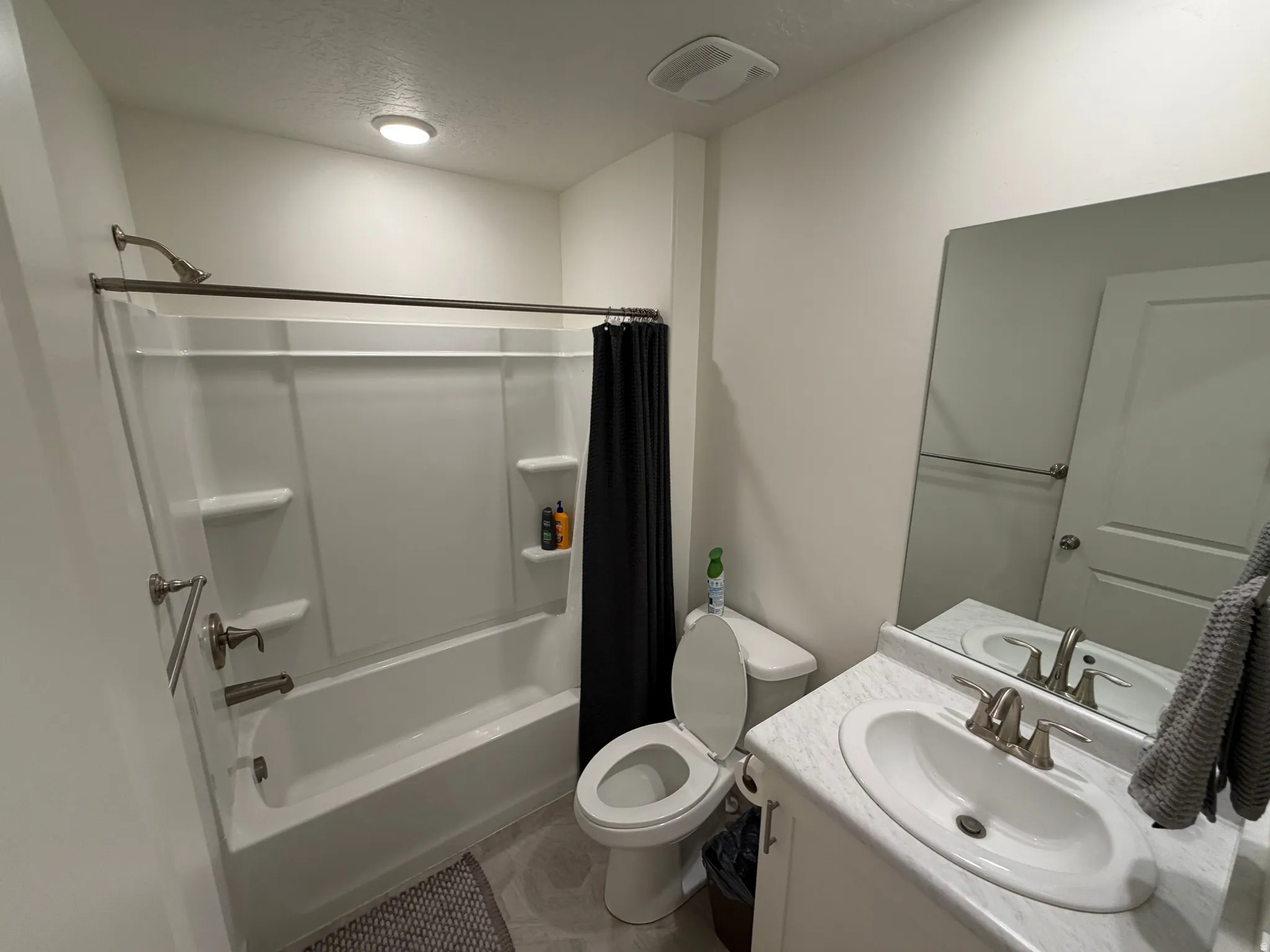Full bathroom featuring a white tub/shower combination with brushed nickel fixtures, a single vanity with an integrated sink, a large wall-mounted mirror, and a toilet