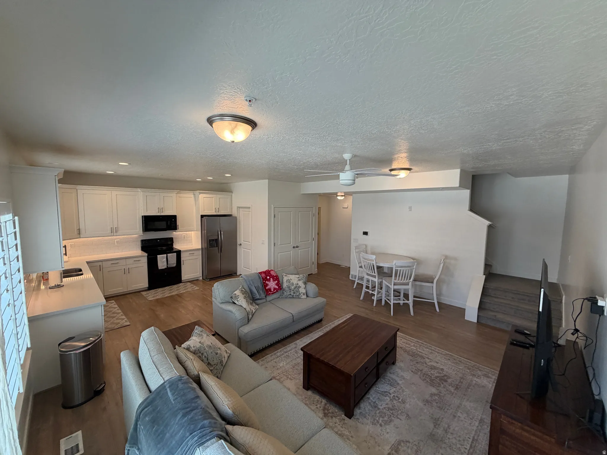 Open-concept living area featuring wood-finish flooring, recessed lighting, white cabinetry, stainless steel appliances, and a ceiling fan