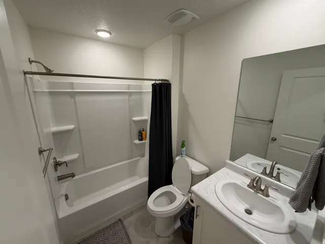 Full bathroom featuring a white tub/shower combination with brushed nickel fixtures, a single vanity with an integrated sink, a large wall-mounted mirror, and a toilet