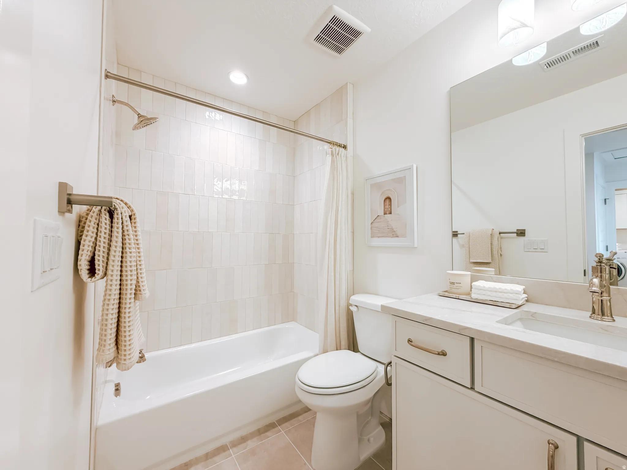 Bathroom featuring a built-in tub with shower, vertical tile surround, and a single vanity with stone countertop