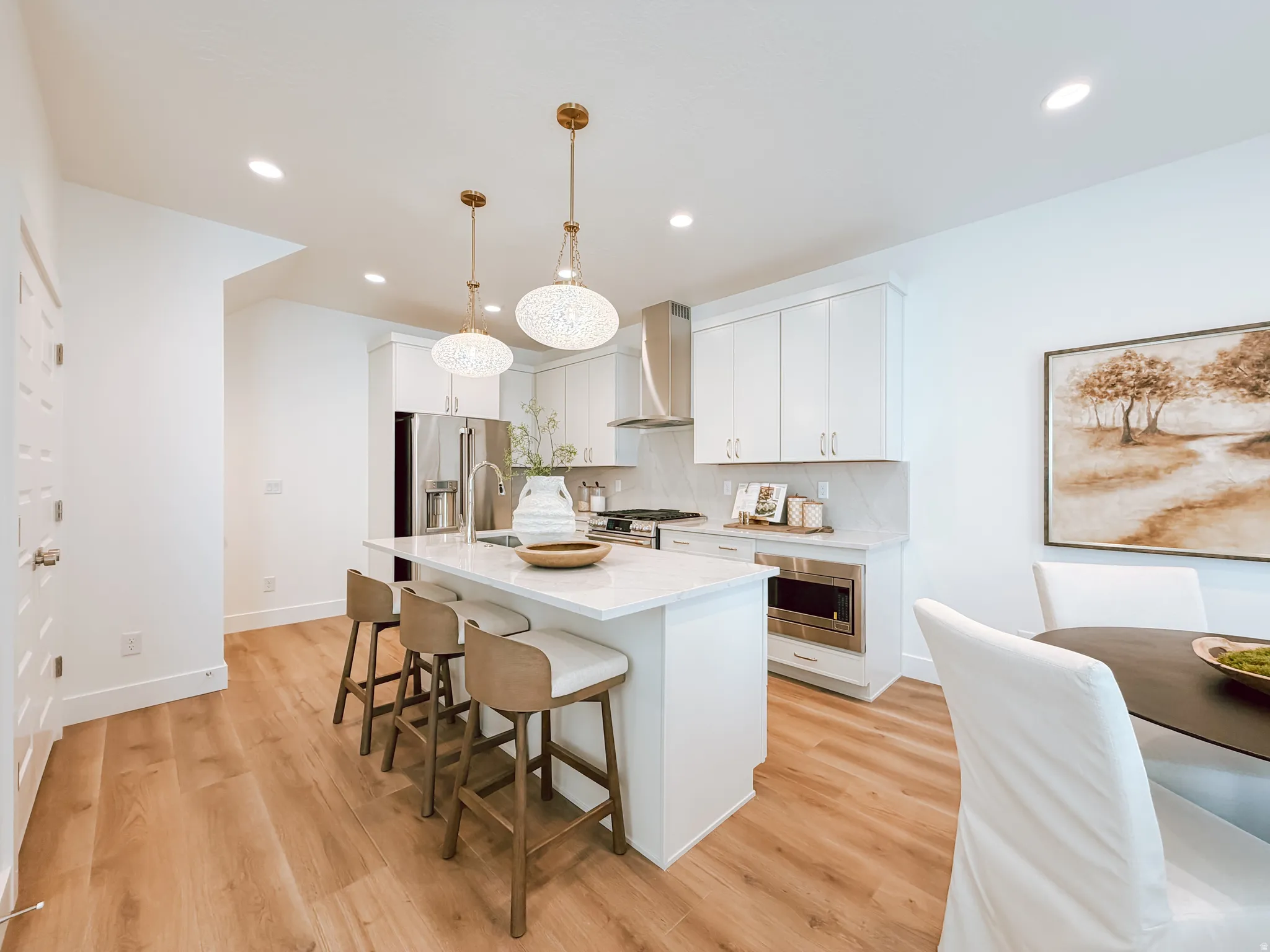 Modern kitchen featuring a central island with seating, white shaker cabinetry, stainless steel appliances, and wood-finish flooring