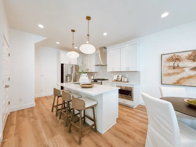Modern kitchen featuring a central island with seating, white shaker cabinetry, stainless steel appliances, and wood-finish flooring