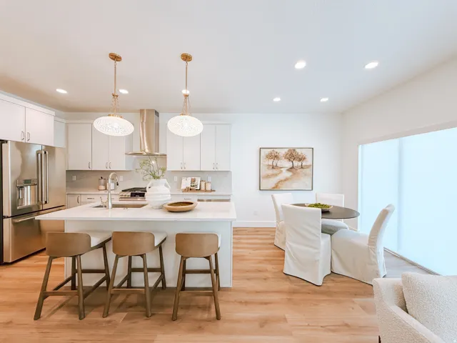 Open-concept kitchen and dining area featuring a large center island with seating, stainless steel appliances, white cabinetry, and wood-finish flooring