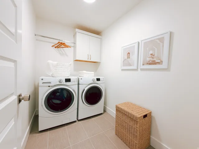 Dedicated laundry space featuring a front-loading washer and dryer, upper cabinetry with wood-finish shelving, an integrated hanging rod, and large format tile flooring