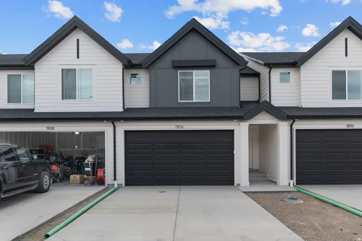 Contemporary townhome exterior featuring an attached garage, white horizontal siding, dark gray accents, a black shingle roof, and multiple windows