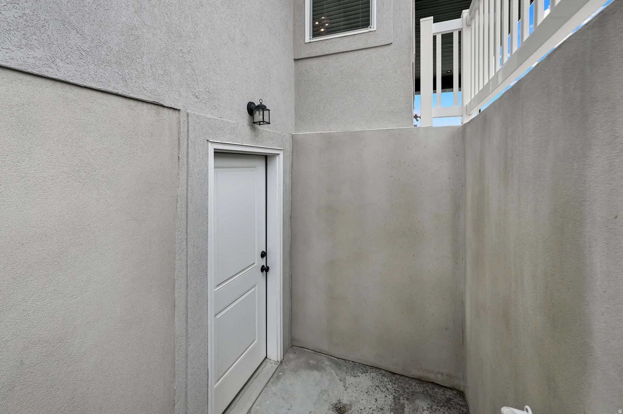 White paneled door, black lantern-style wall sconce, and textured exterior finish