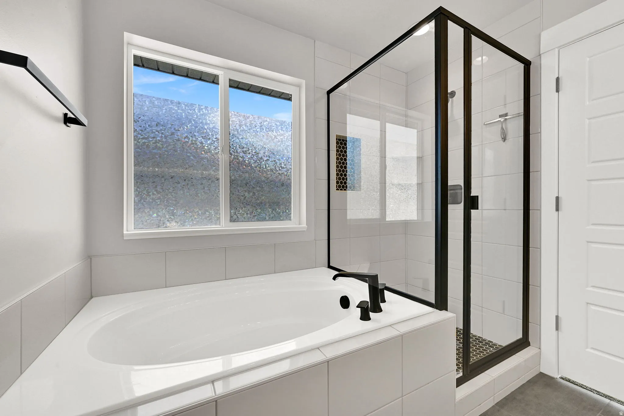 Built-in corner bathtub, black-framed glass shower enclosure, and tiled shower walls with mosaic accent
