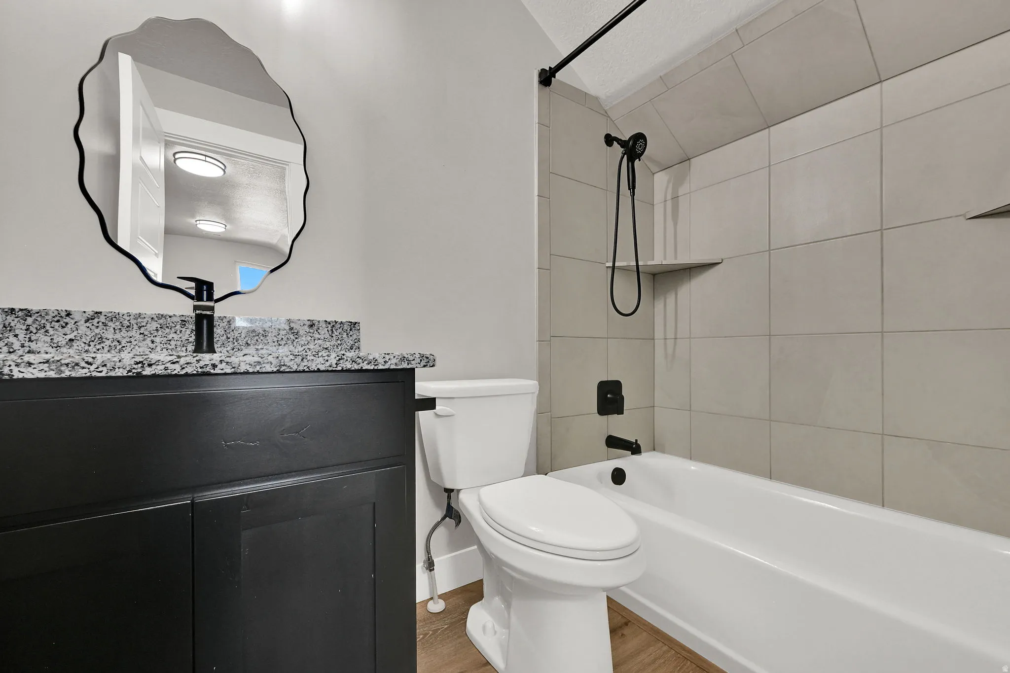 Black vanity with granite-style countertop, matte black faucet, and organic-shaped mirror