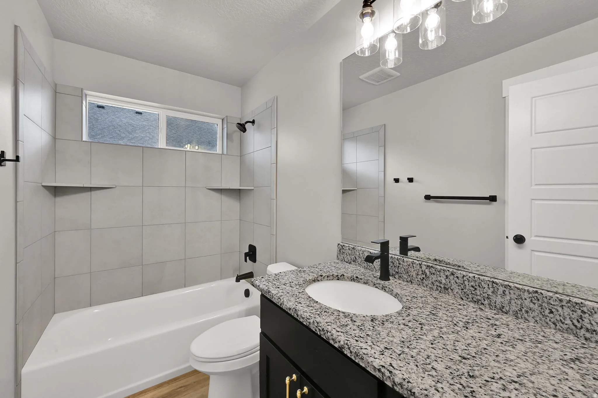 Bathroom featuring a white bathtub, light-toned tile surround with integrated shelving, and a vanity with a speckled countertop and dark cabinetry