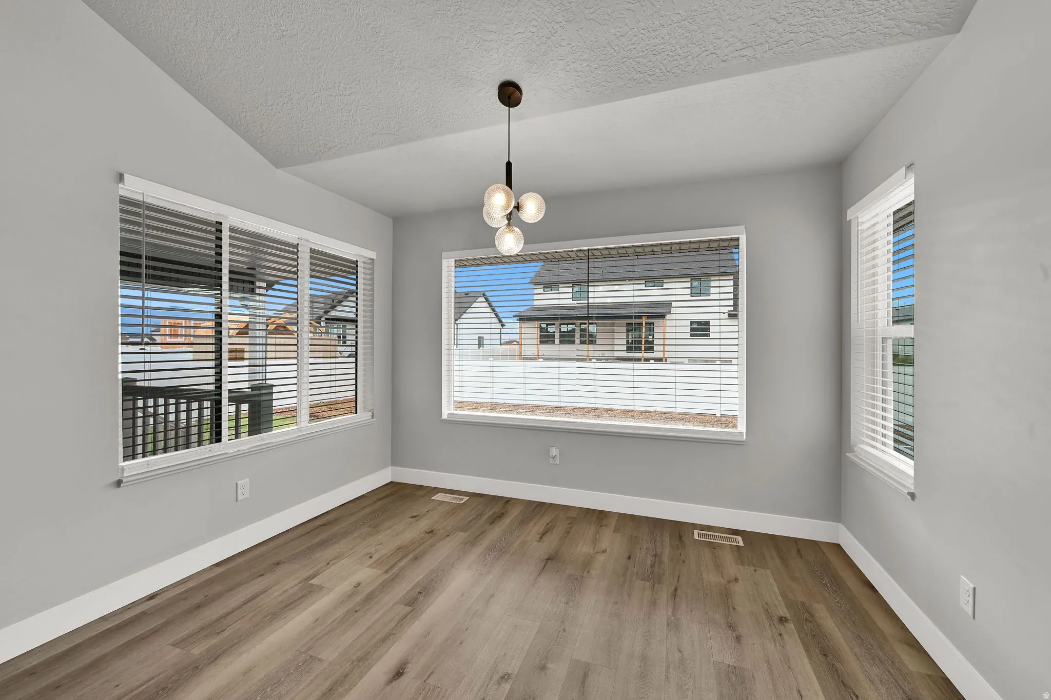 Vaulted ceiling with a modern chandelier, wood-finish flooring, and multiple windows with blinds
