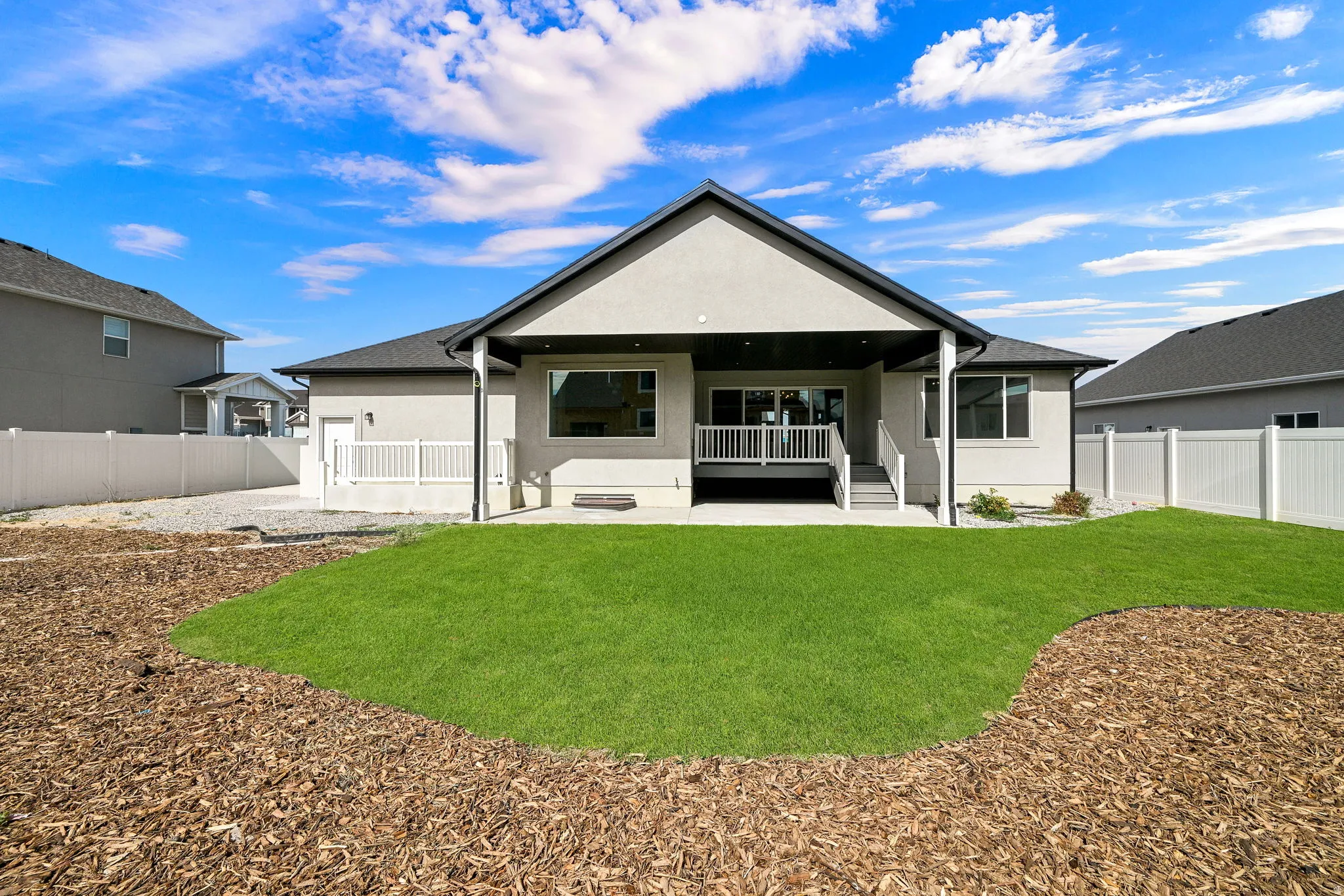 Expansive backyard with a manicured lawn, wood chip landscaping, and a covered patio with a deck