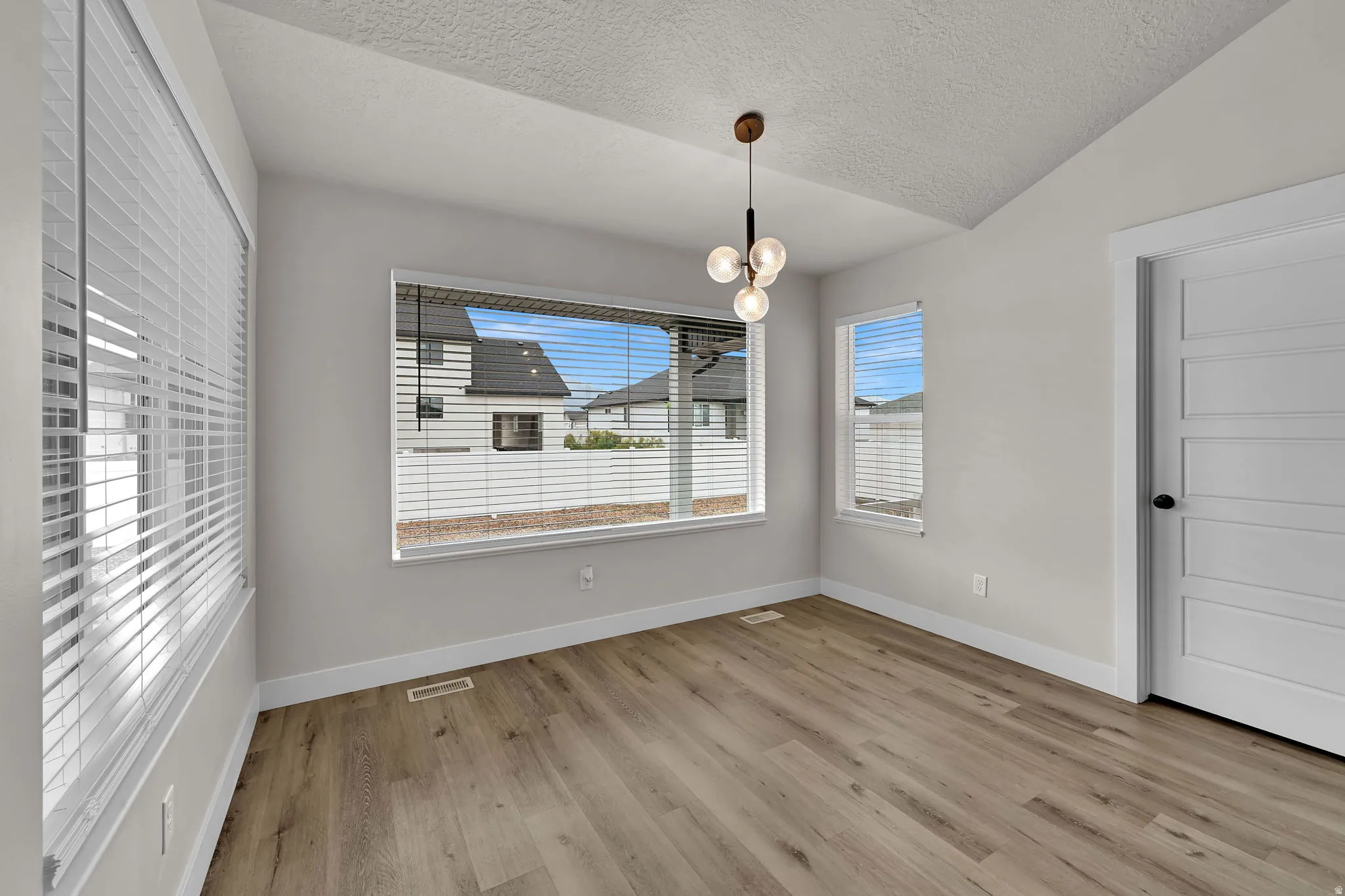 Vaulted ceiling with a modern spherical chandelier, wood-finish flooring, and multiple windows with blinds