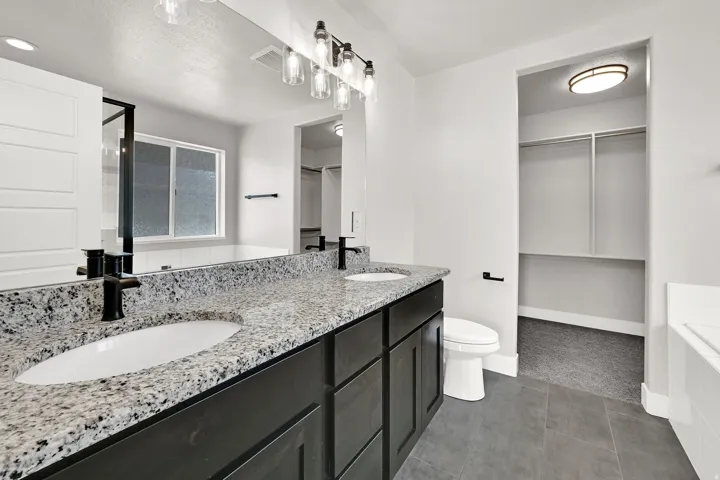 Dual vanity with stone countertop and integrated sinks, matte black fixtures, recessed lighting, and a walk-in closet with built-in shelving