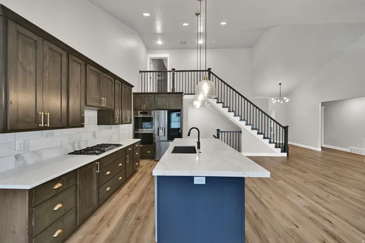 Expansive kitchen featuring a large central island with sink, dark wood-finish cabinetry, light-toned countertops, and a full tile backsplash