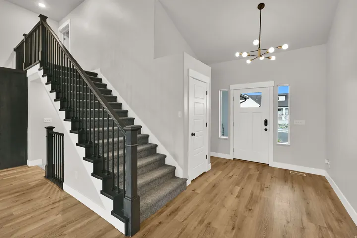 Spacious entryway featuring wood-finish flooring, a contemporary chandelier, and a white paneled door with glass inserts