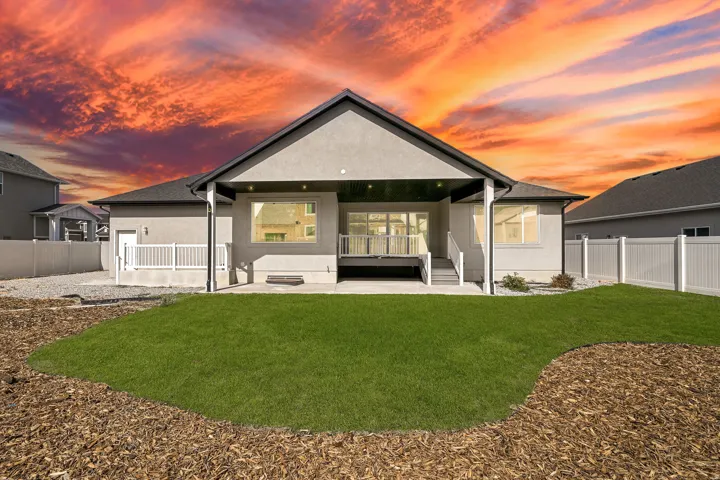 Spacious backyard featuring a manicured lawn, a covered concrete patio, an elevated deck with white railings, and a white vinyl privacy fence