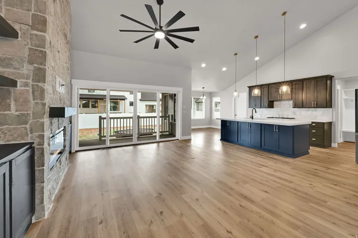 Vaulted ceiling, stone-clad fireplace, wood-finish flooring, sliding glass door, and a kitchen island with pendant lighting