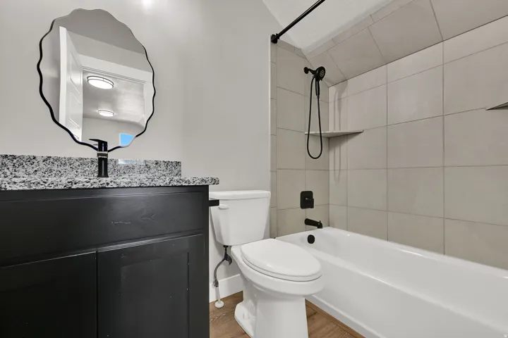 Black vanity with granite-style countertop, matte black faucet, and organic-shaped mirror