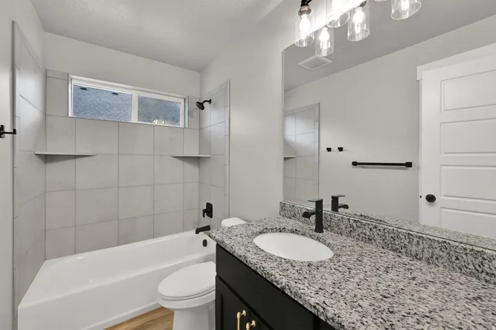 Bathroom featuring a white bathtub, light-toned tile surround with integrated shelving, and a vanity with a speckled countertop and dark cabinetry