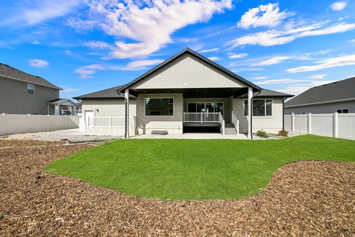 Expansive backyard with a manicured lawn, wood chip landscaping, and a covered patio with a deck