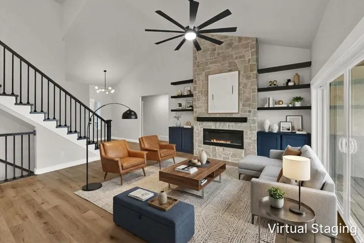 Vaulted ceiling, stone-clad fireplace with built-in shelving, wood-finish flooring, staircase with metal balusters, and sliding glass doors