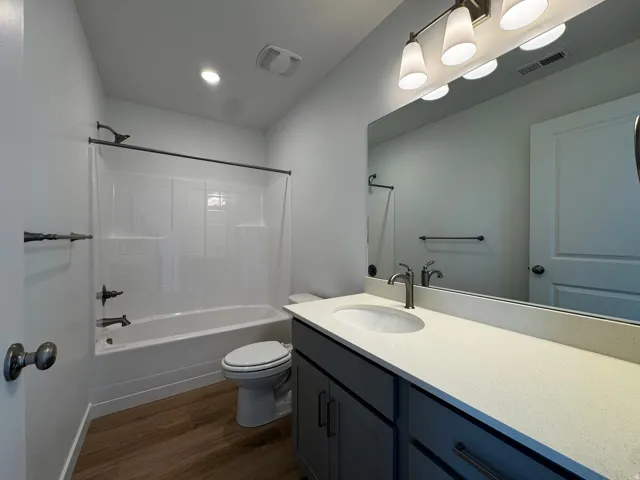 Bathroom featuring a white tub/shower combination, dark bronze fixtures, a vanity with a light-colored countertop, and wood-finish flooring