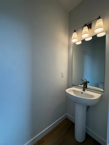 Pedestal sink featuring a single-hole faucet with a dark finish, illuminated by a three-light vanity fixture