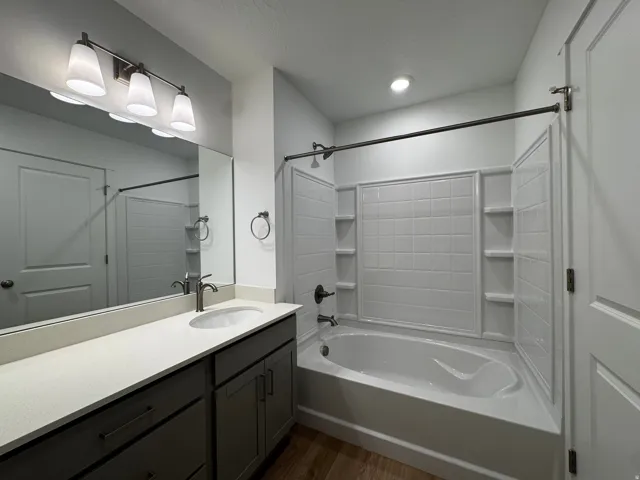 Bathroom featuring a white bathtub with a tiled shower surround, a vanity with a light-colored countertop, and dark-finished cabinetry