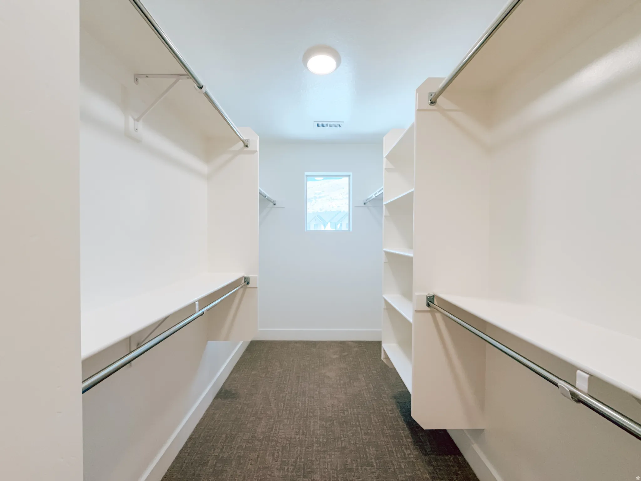 Spacious walk-in closet featuring white shelving units, multiple hanging rods, and recessed lighting